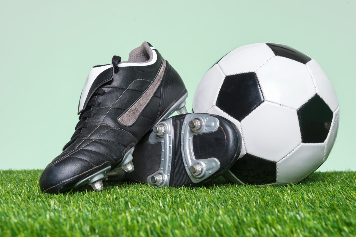 Ballon de football et chaussures à crampons noires sur une pelouse Image