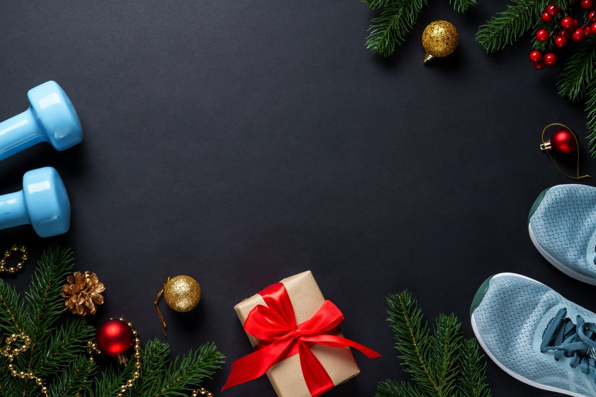 Haltères, baskets de running et cadeau de Noël entourés de branches de sapin sur fond noir Image