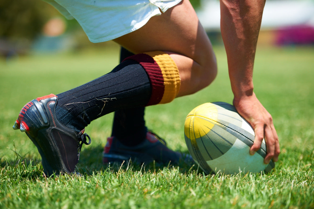 Joueur de rugby qui pose le ballon sur la pelouse, crampons aux pieds Image
