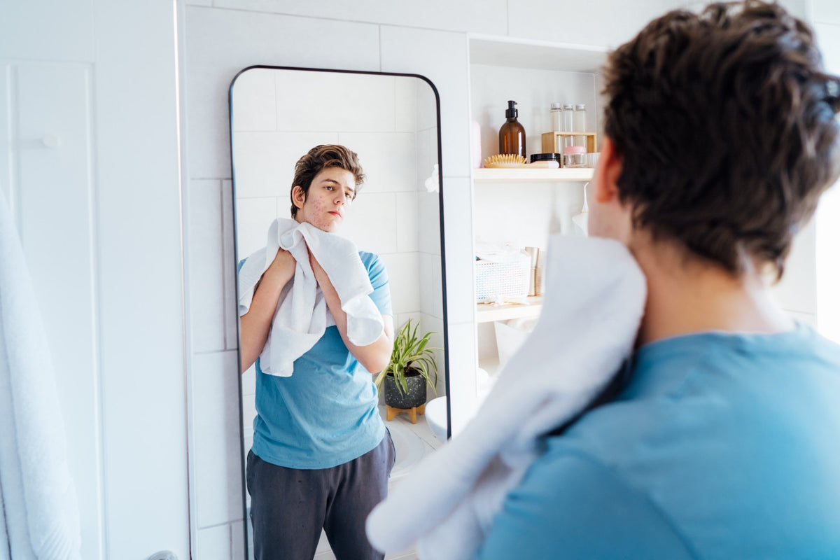 Jeune homme observant les boutons d'acné sur son visage dans le miroir de la salle de bain Image