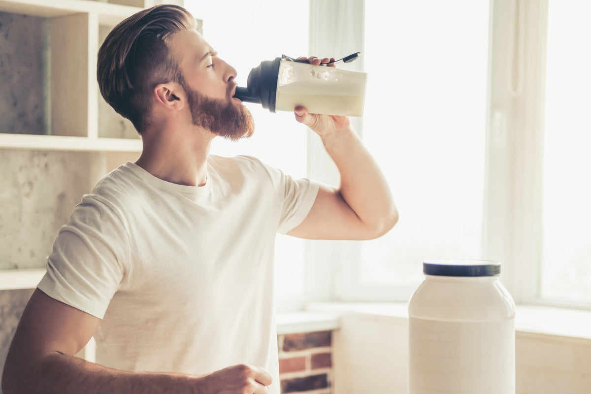 Homme barbu buvant un shake de whey protéine dans sa cuisine Image