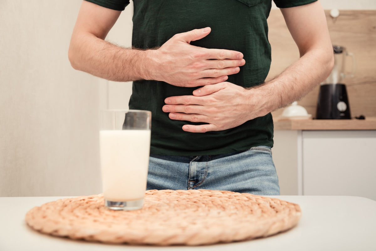 Homme se tenant le ventre devant un verre de lait, symptômes d'intolérance au lactose Image